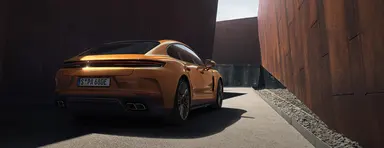 Rear shot of the new Panamera Turbo E-Hybrid in Madeira Gold Metallic standing on the road between modern buildings.